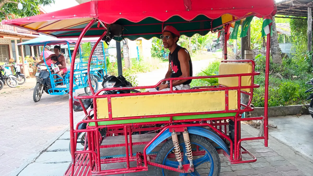 Man waiting for customers in a red and yellow motorized tricycle taxi