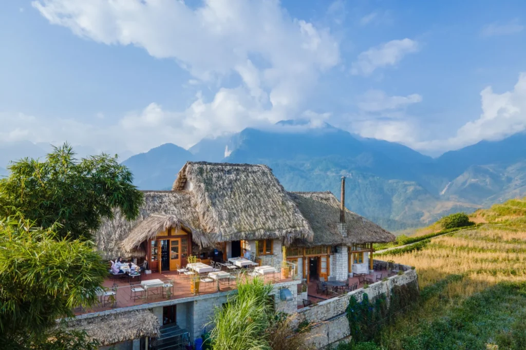 Thatched-roof lodge with a terrace overlooking mountains and clouds