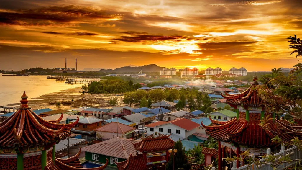 Sunset over a coastal town with ornate temple rooftops in the foreground