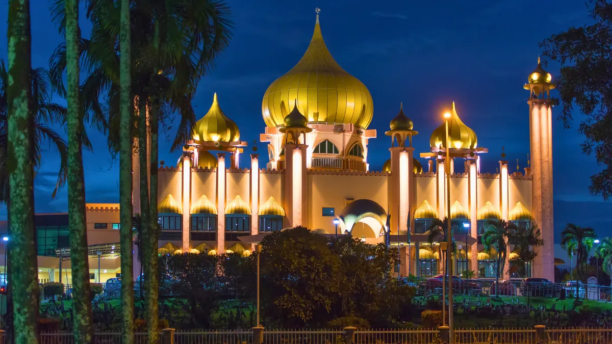 Illuminated mosque with golden domes and palm trees at night