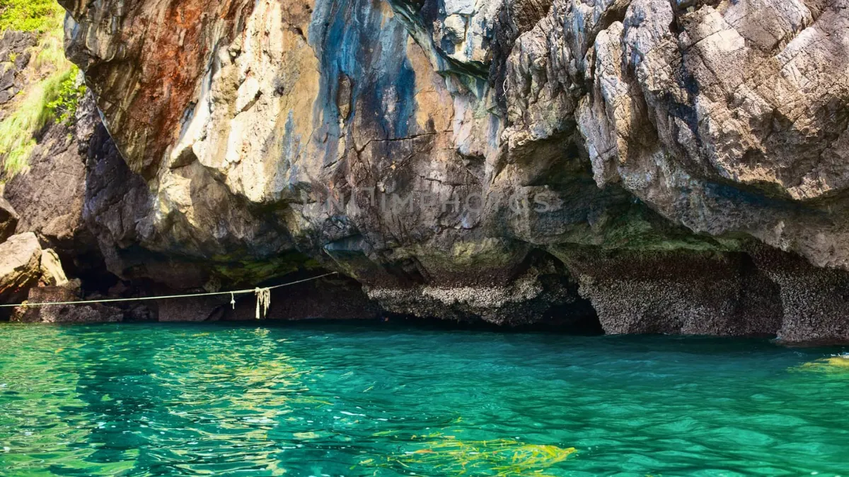 Rocky cliff over clear turquoise water with a rope stretched across the cove
