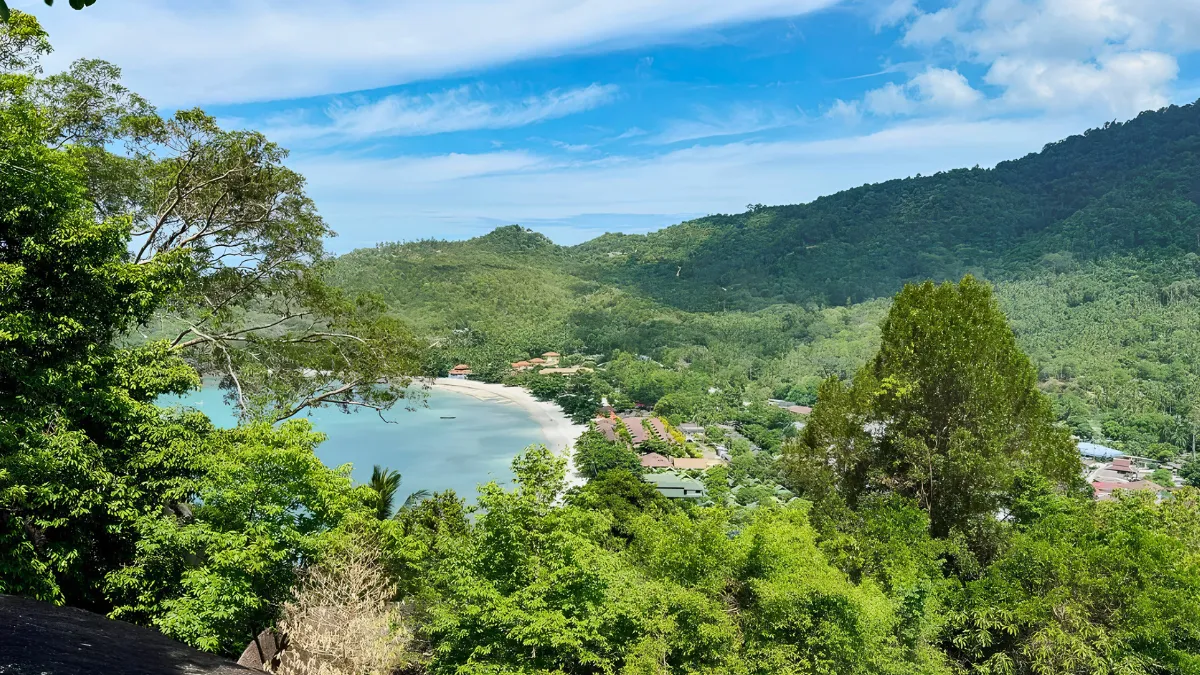 Tropical bay with a sandy beach, green hills, and dense forest under a blue sky