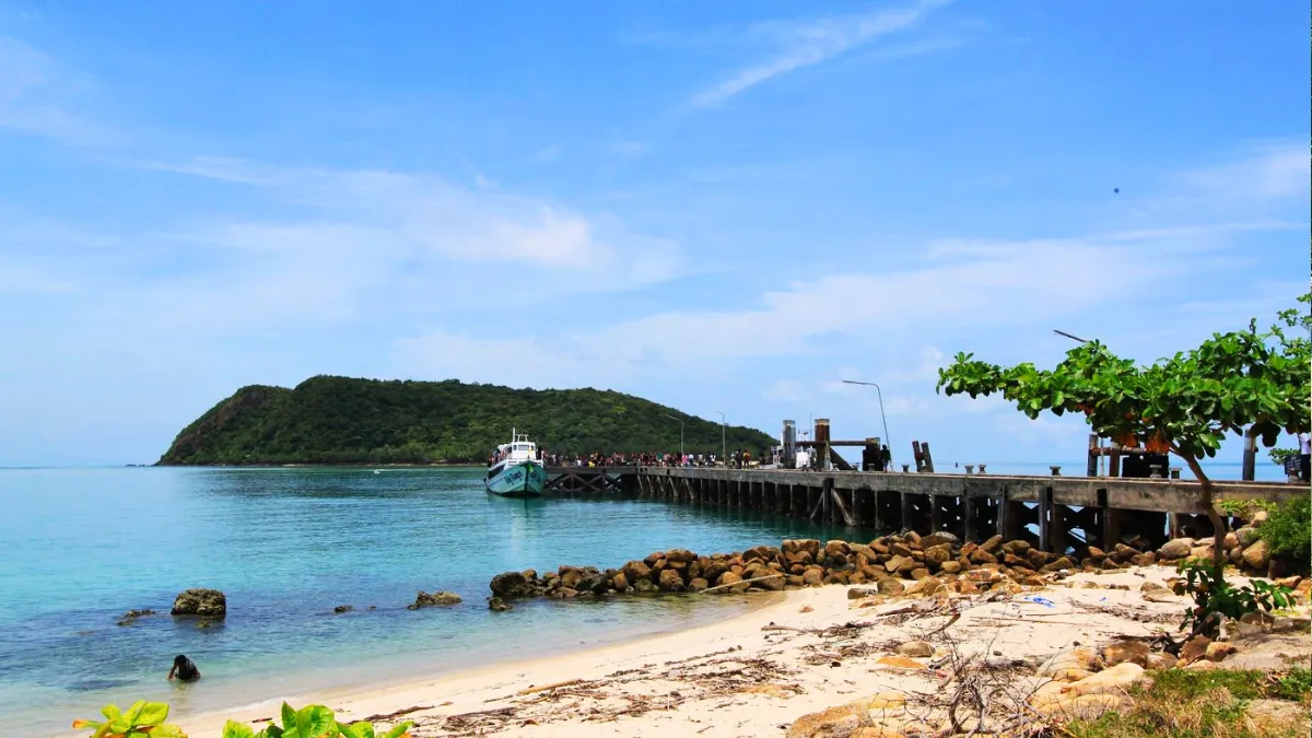 Tropical beach with a pier, boat, and green island under a blue sky
