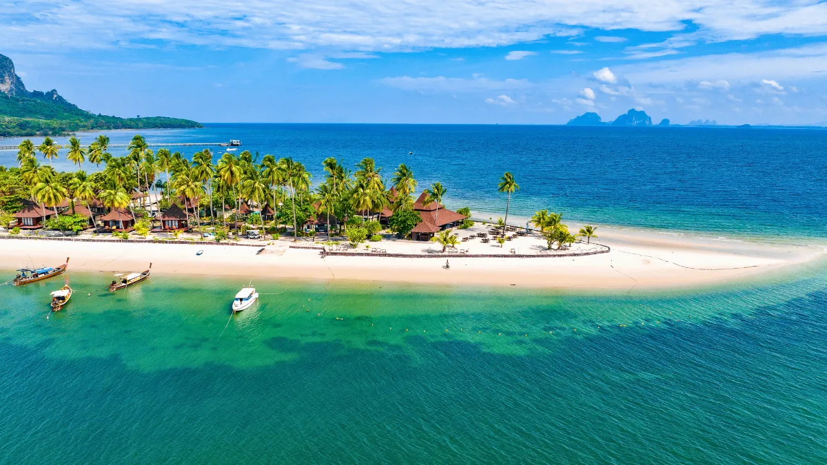 A tropical island resort with palm trees, white sand beach, and boats in clear blue water