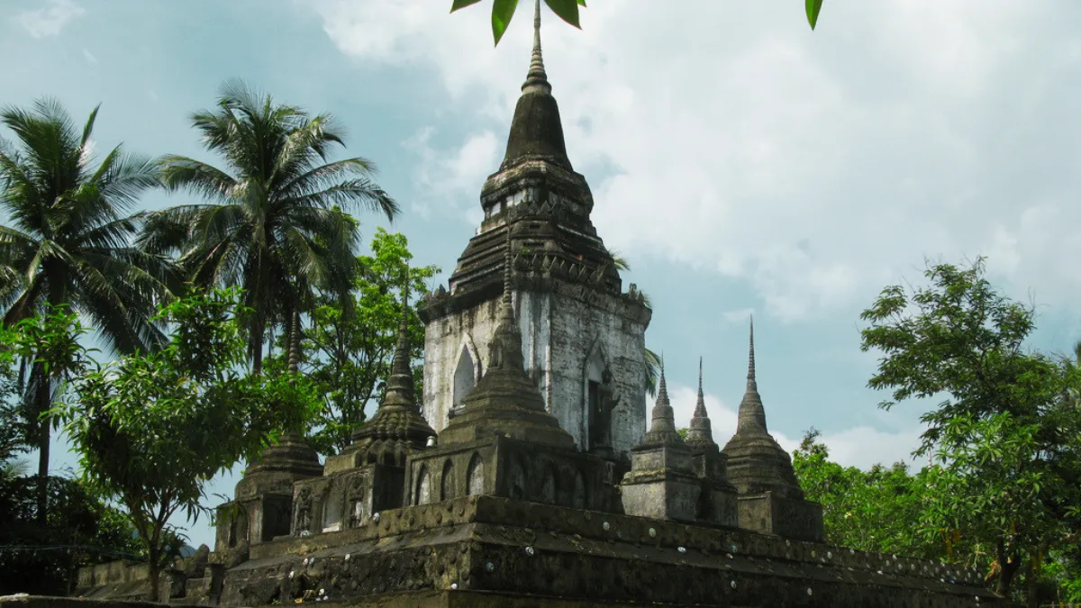 Ancient stone temple with a tall central spire surrounded by palm trees