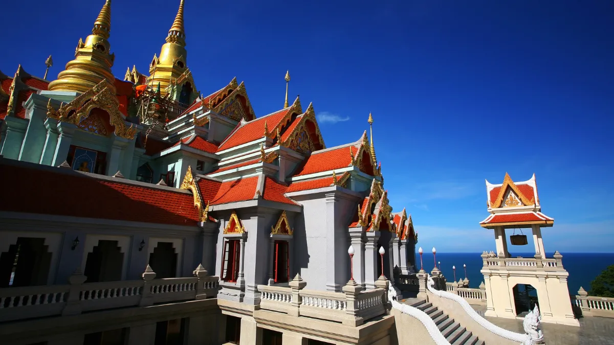 Temple complex with ornate golden spires and red roofs overlooking the sea