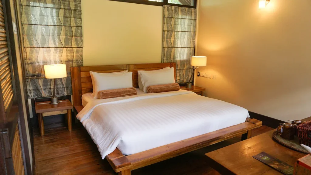 A cozy hotel bedroom with a wooden bed, bedside lamps, and patterned curtains