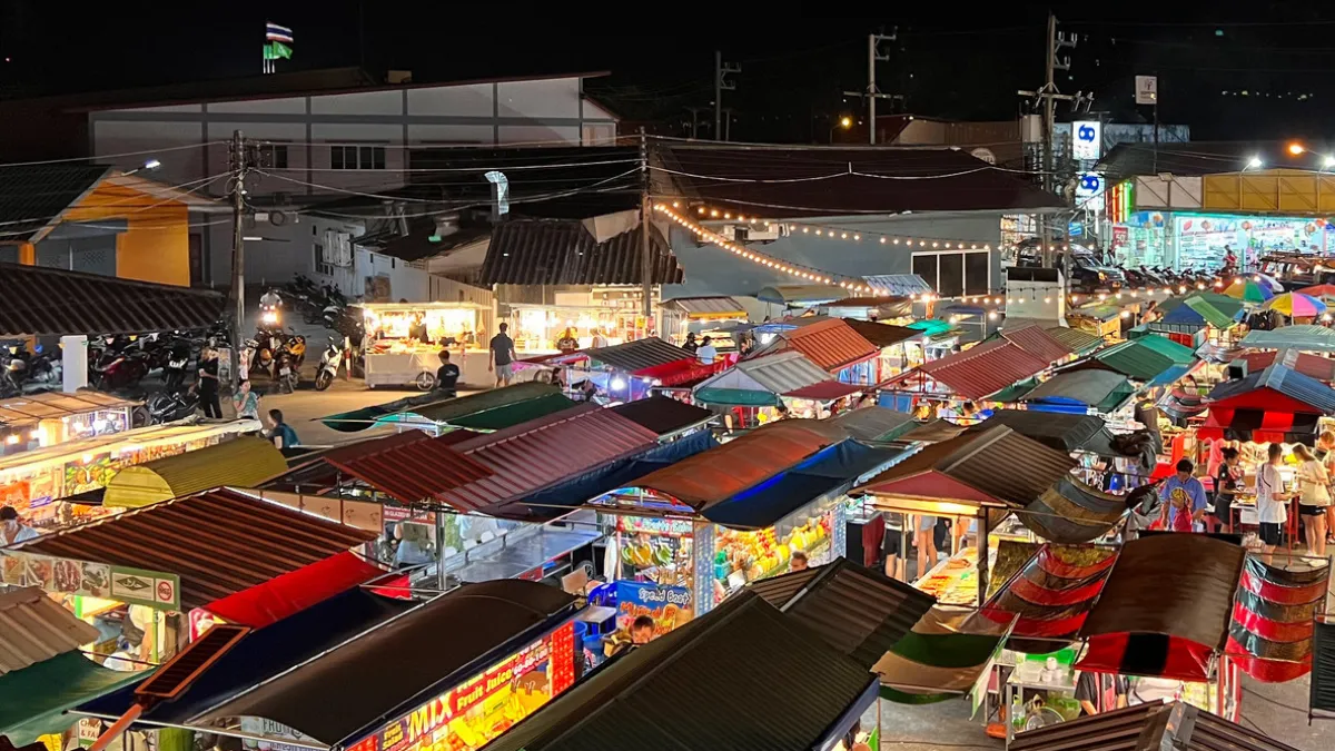 Night market with rows of colorful vendor stalls and crowds under bright lights