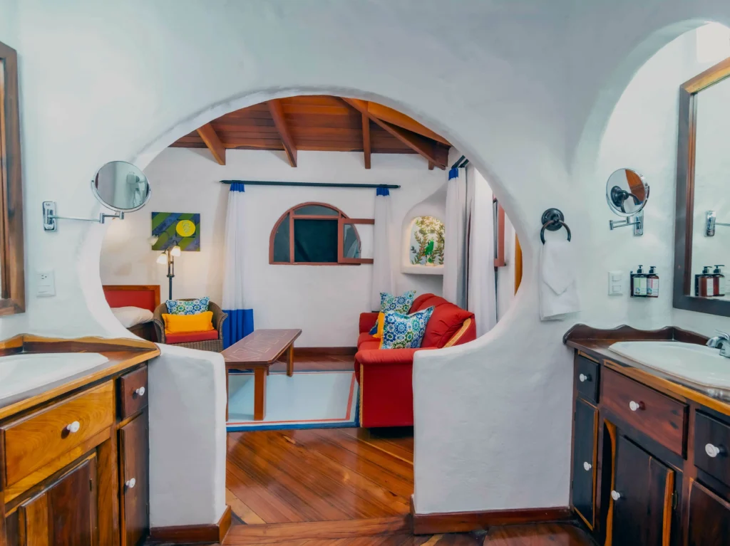 A cozy bathroom with an arched opening into a sitting area, red sofa, and wooden ceiling beams