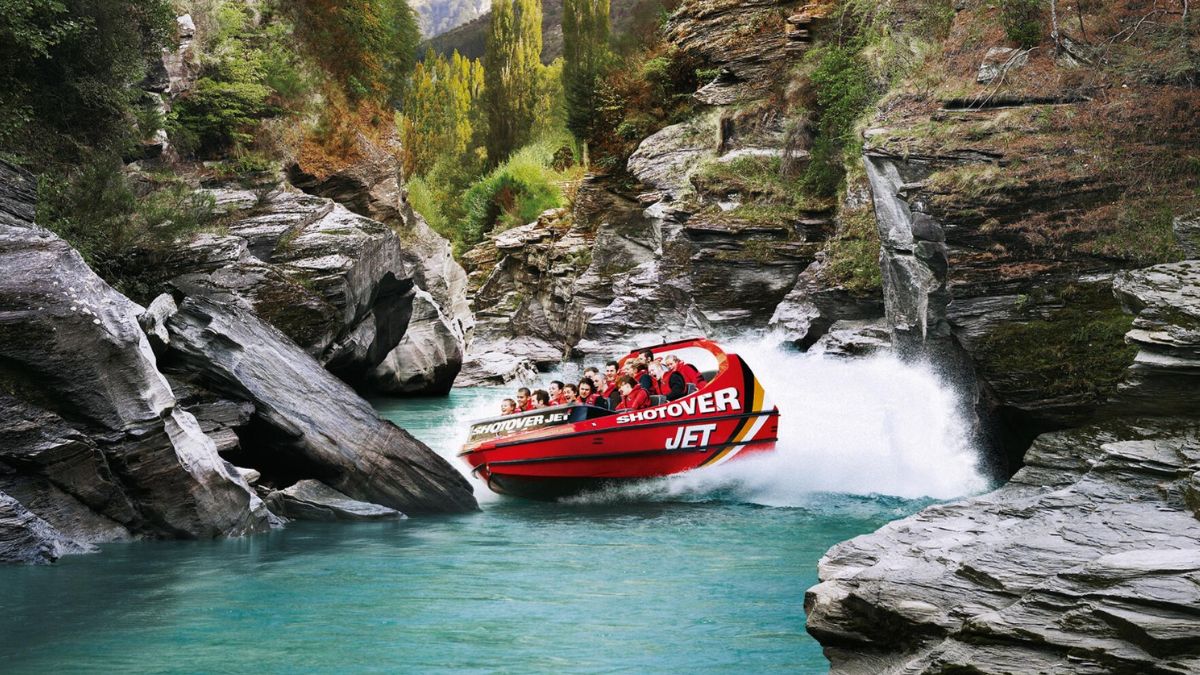 Red jet boat carrying passengers through a rocky canyon, spraying water