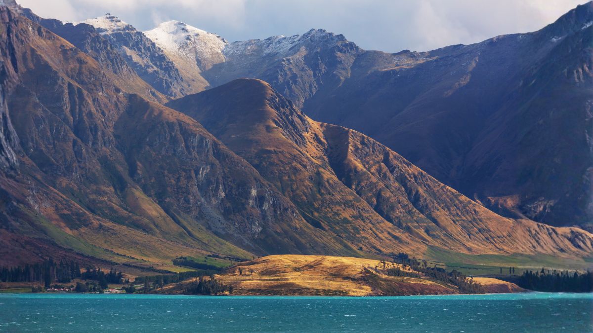 Mountain range with rugged, sunlit slopes and snow-capped peaks beside a turquoise lake