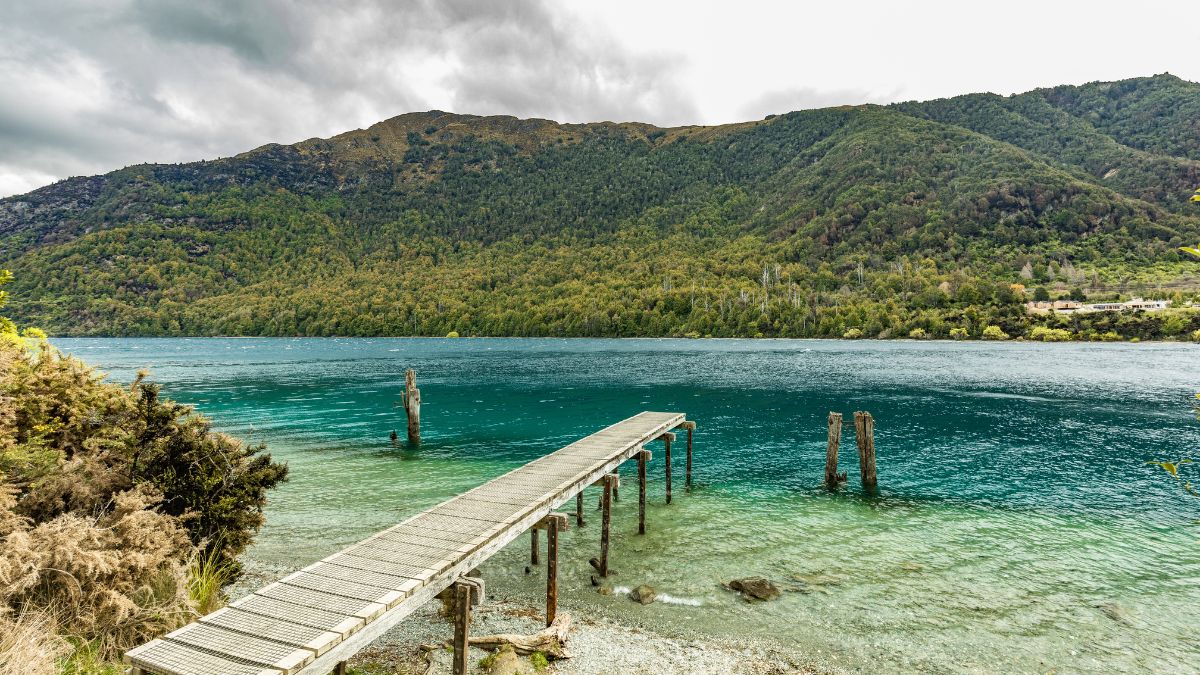 Wooden pier extending into a turquoise lake, with forested mountains under a cloudy sky - Bobs Cove, Queenstown Travel Guide, New Zealand