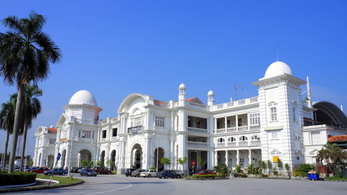 White domed colonial-style building with arched balconies and palm trees under a clear blue sky
