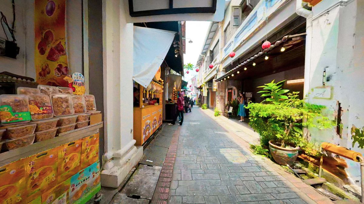 Narrow pedestrian market alley lined with food stalls, shops, hanging red lanterns, and potted plants