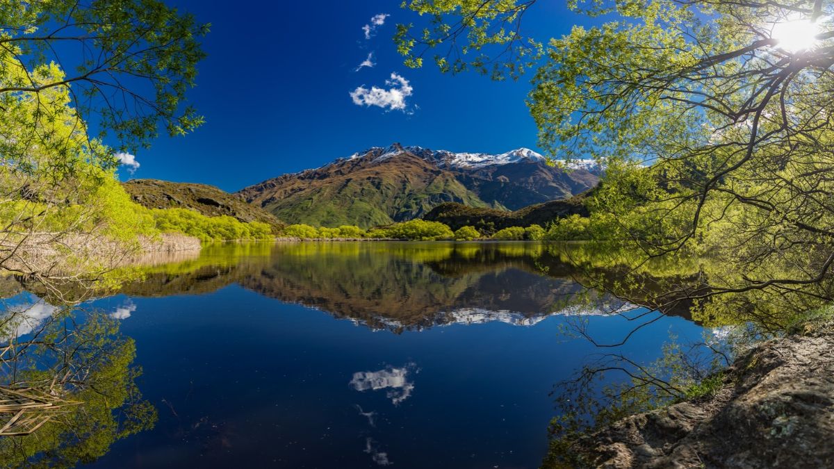 Mountain lake reflecting snow-capped mountains, trees, and a blue sky