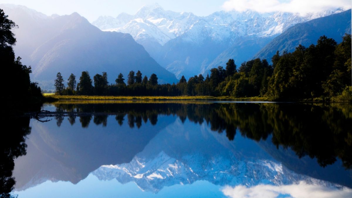 Snow-capped mountains reflected in a calm lake bordered by forest