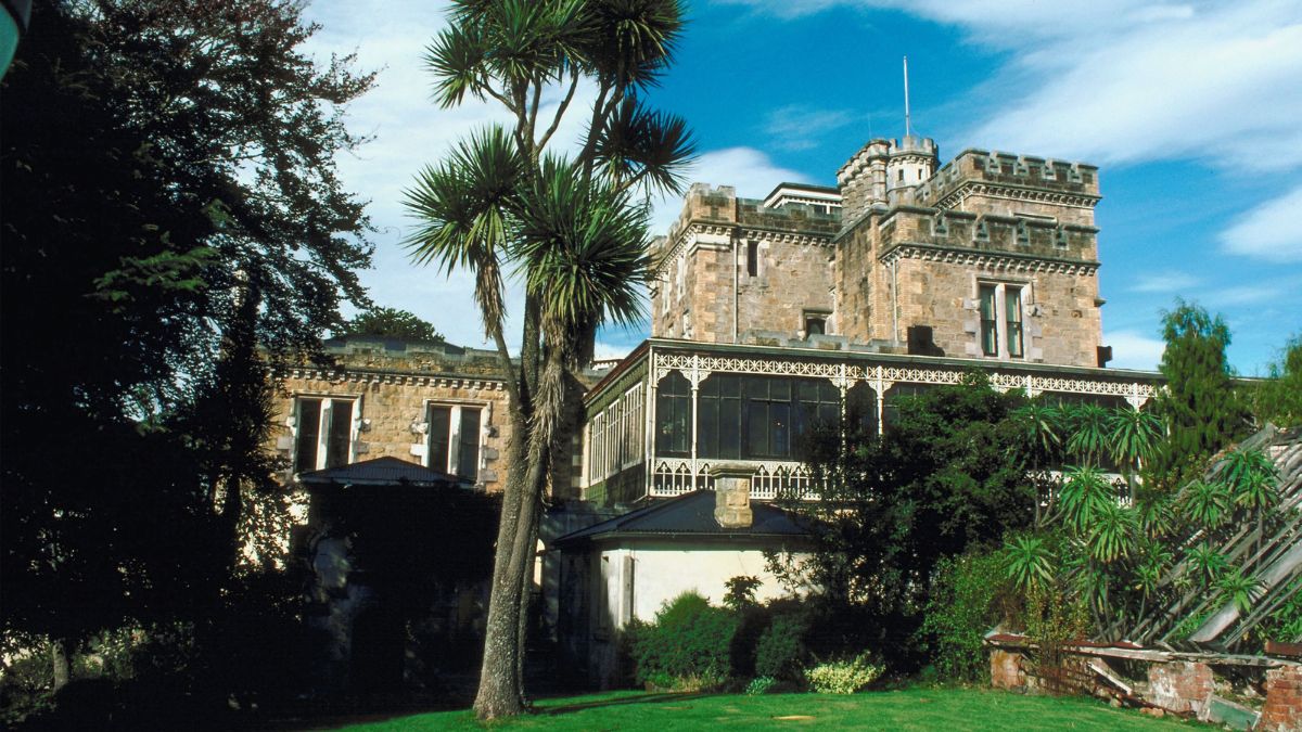 Stone castle-like mansion with an ornate veranda, surrounded by palm trees and gardens
