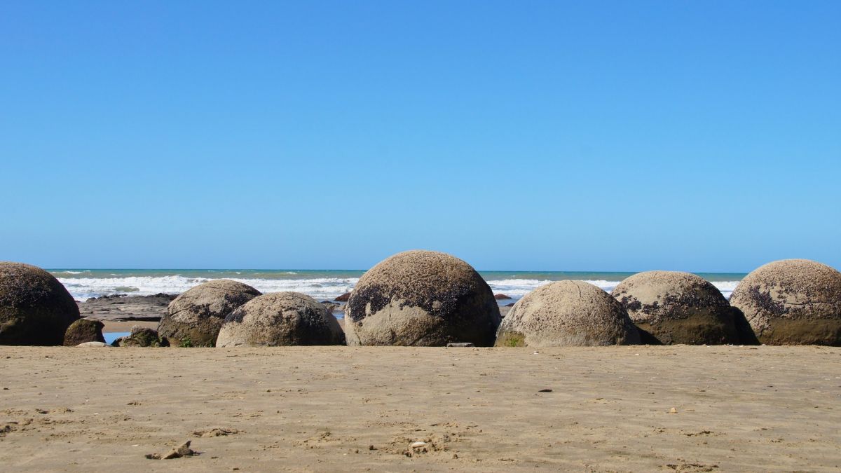 Spherical Moeraki Boulders on a sandy beach with waves and a clear blue sky