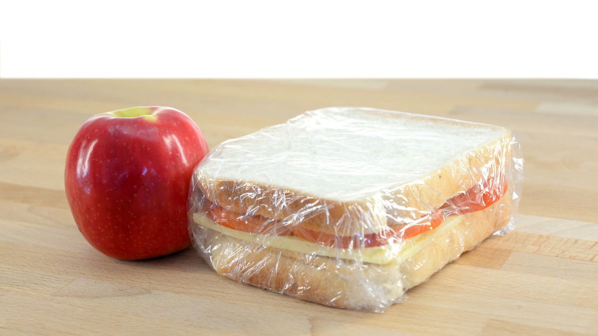 Apple and plastic-wrapped sandwich on a wooden table