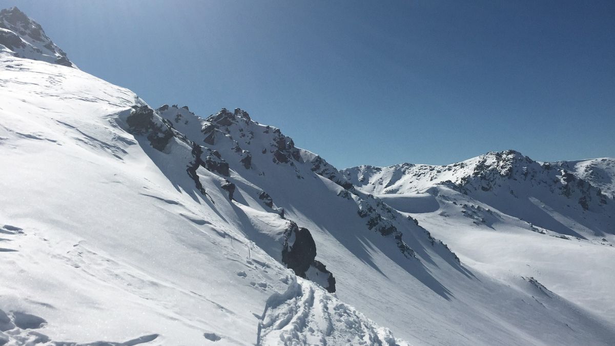 Snow-covered mountain ridges and steep slopes beneath a clear blue sky. The Remarkables, Queenstown Travel Guide