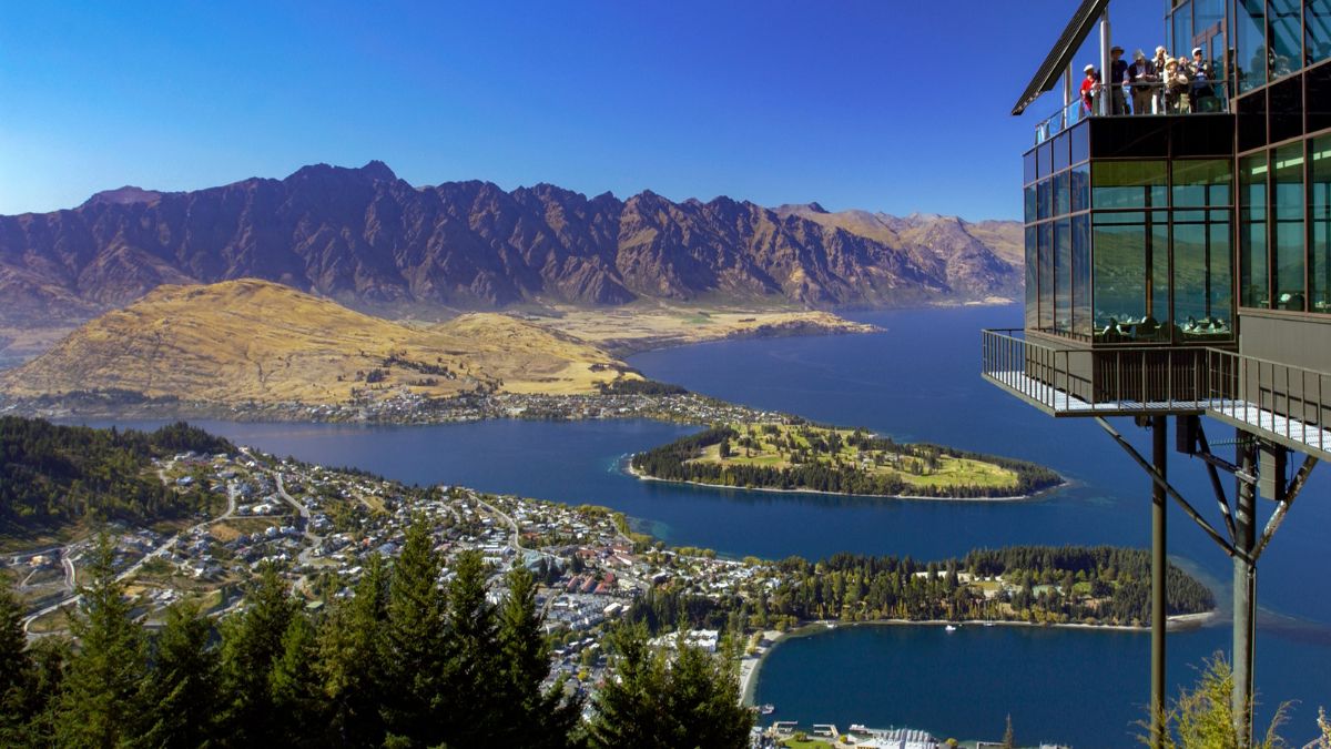 Panoramic view of a lakeside town, blue lake, rugged mountains, and a glass observation building