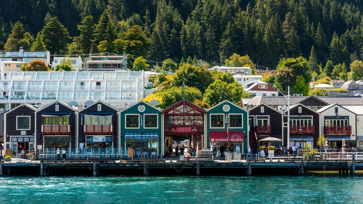 Waterfront shops and restaurants beside turquoise water, backed by forested mountains